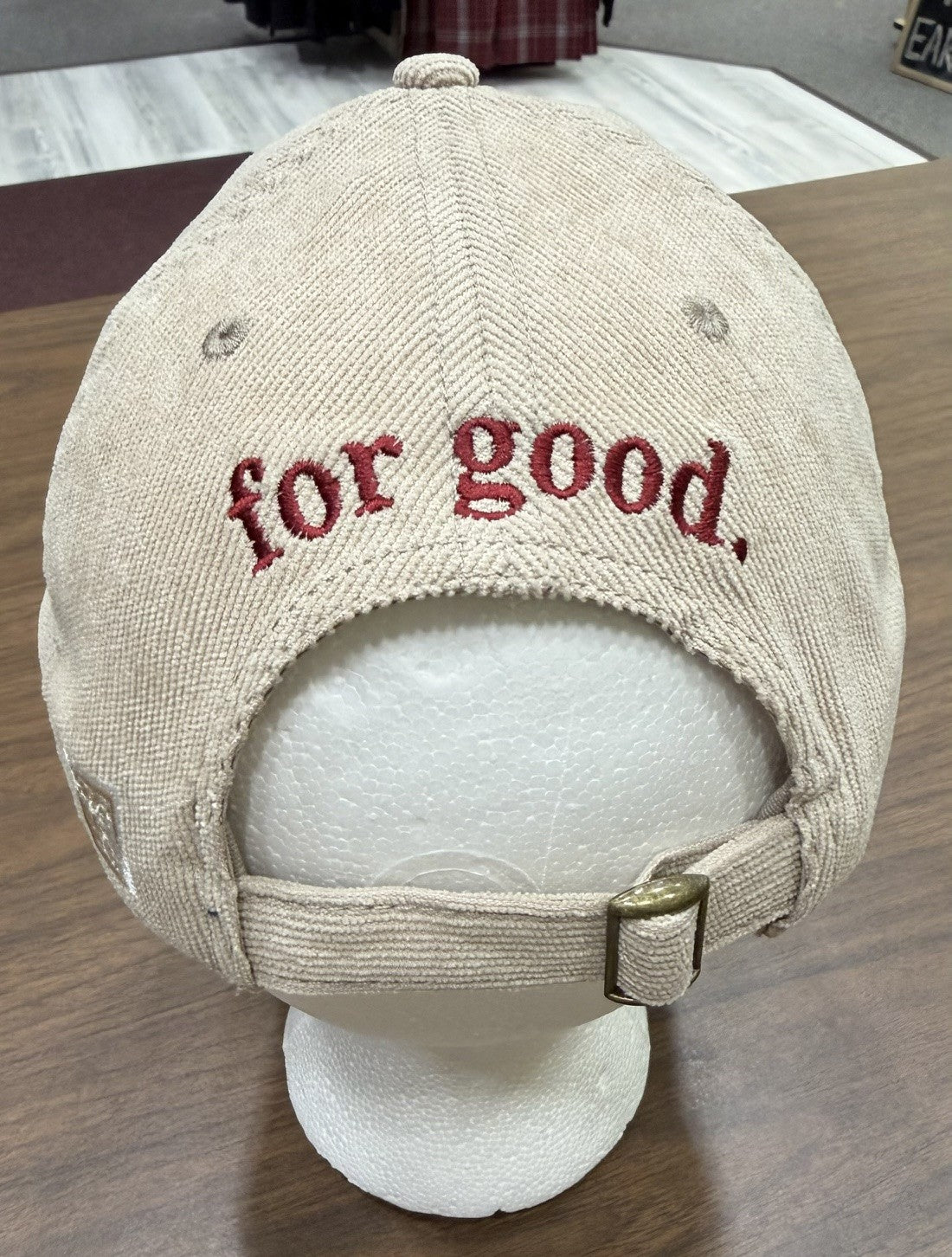 The “for good.” Corduroy Cap, in beige with “for good.” embroidered in red on the back, is displayed on a white mannequin head atop a wooden table.