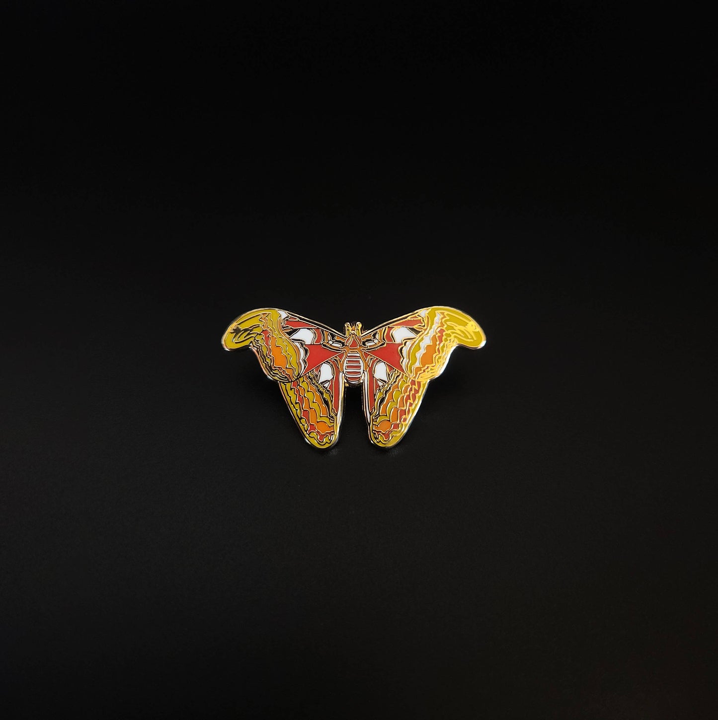 The Atlas Moth Educational Insect Enamel Pin, featuring vibrant yellow, orange, and red patterns, is displayed centered on a solid black background.