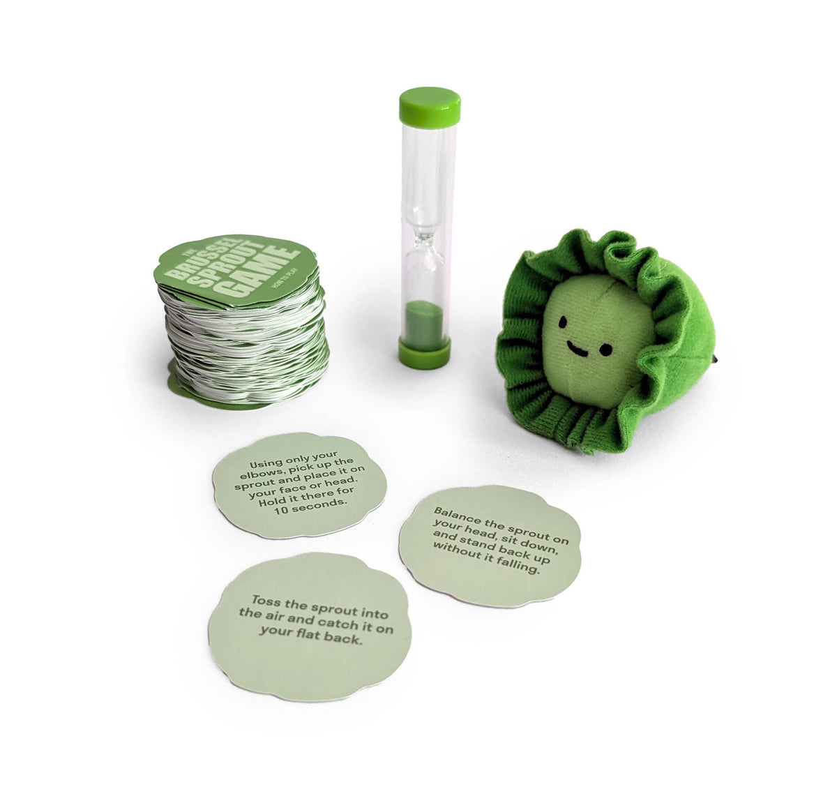 A plush sprout character, a green hourglass timer, and three challenge cards from The Sprout Game | Hilarious Family Party Game laid out on a white surface.