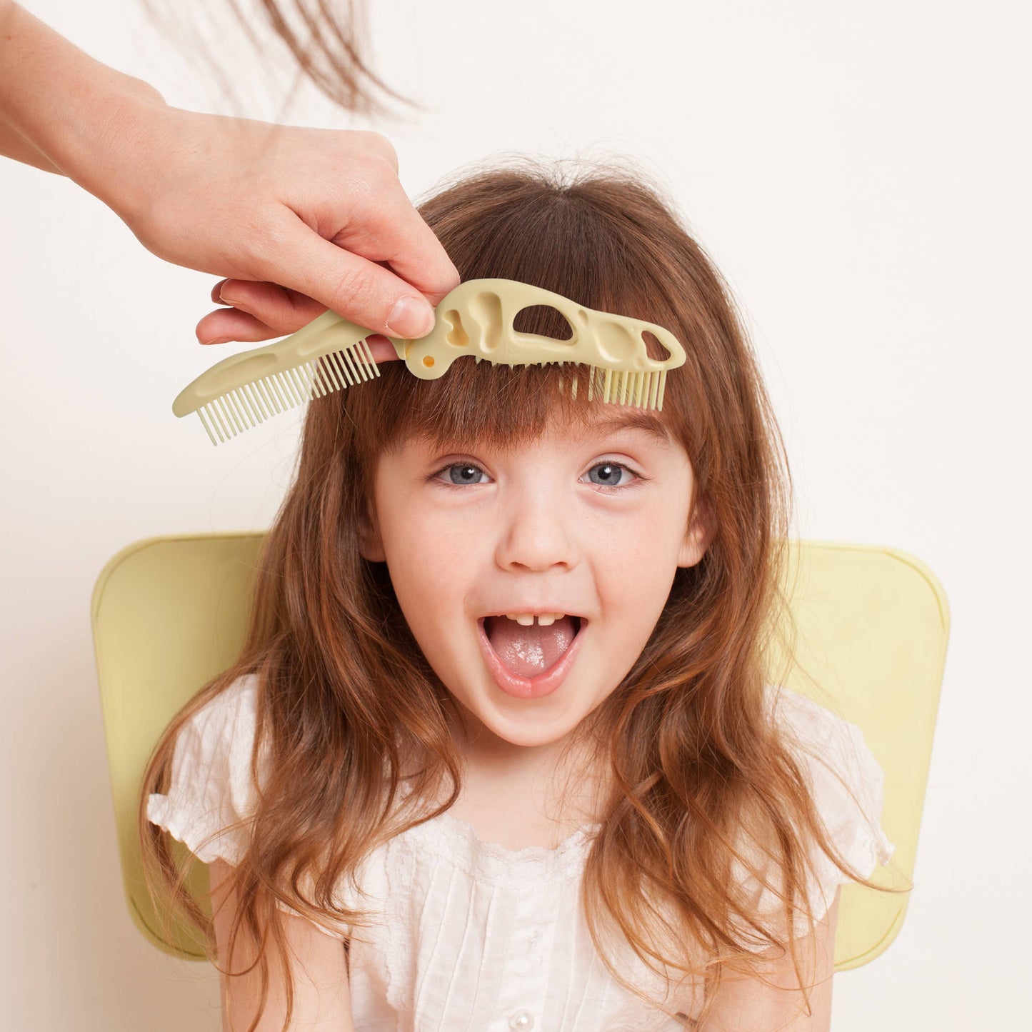 Child's hair being combed with the BoneHEAD dinosaur skull-shaped dual brush and comb