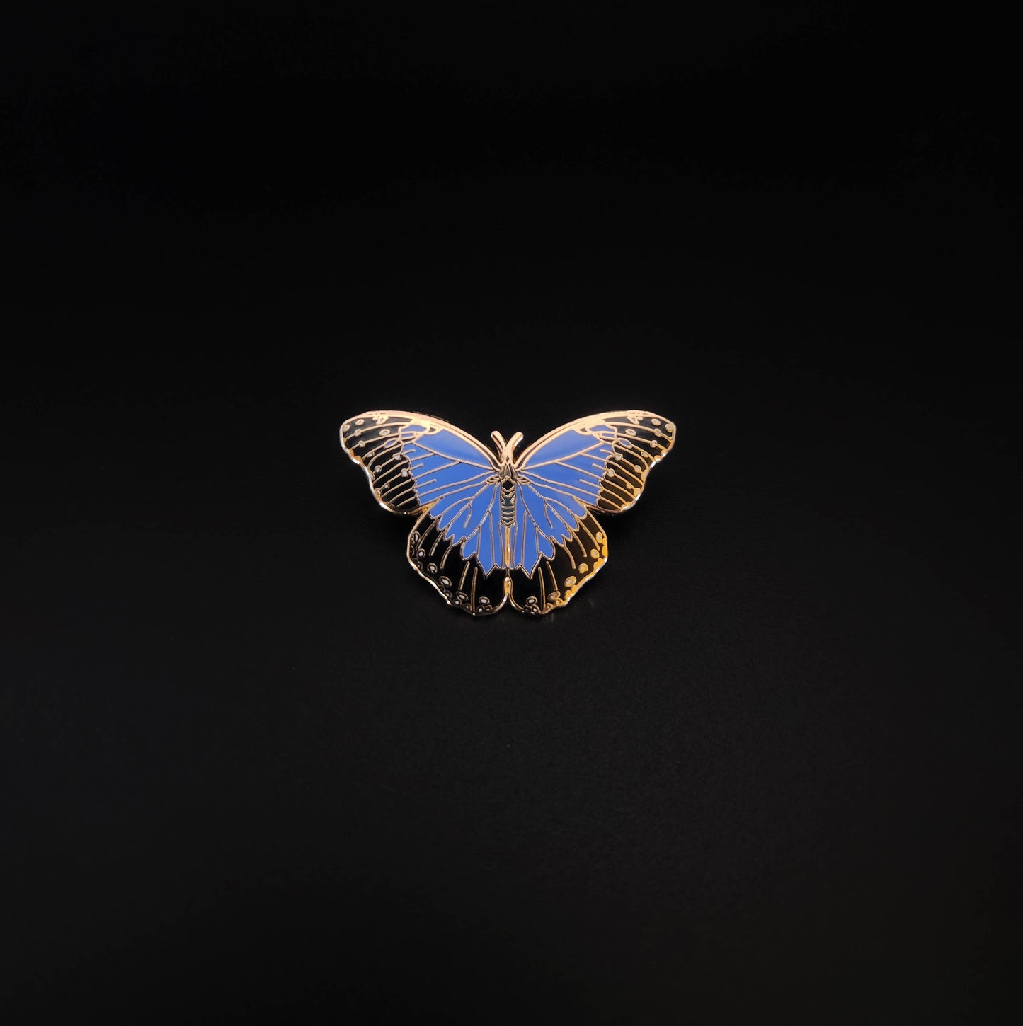 The Blue Morpho Butterfly Educational Insect Enamel Pin, featuring a gold-rimmed design, is centered on a solid black background, making it a striking nature gift for any butterfly lover.