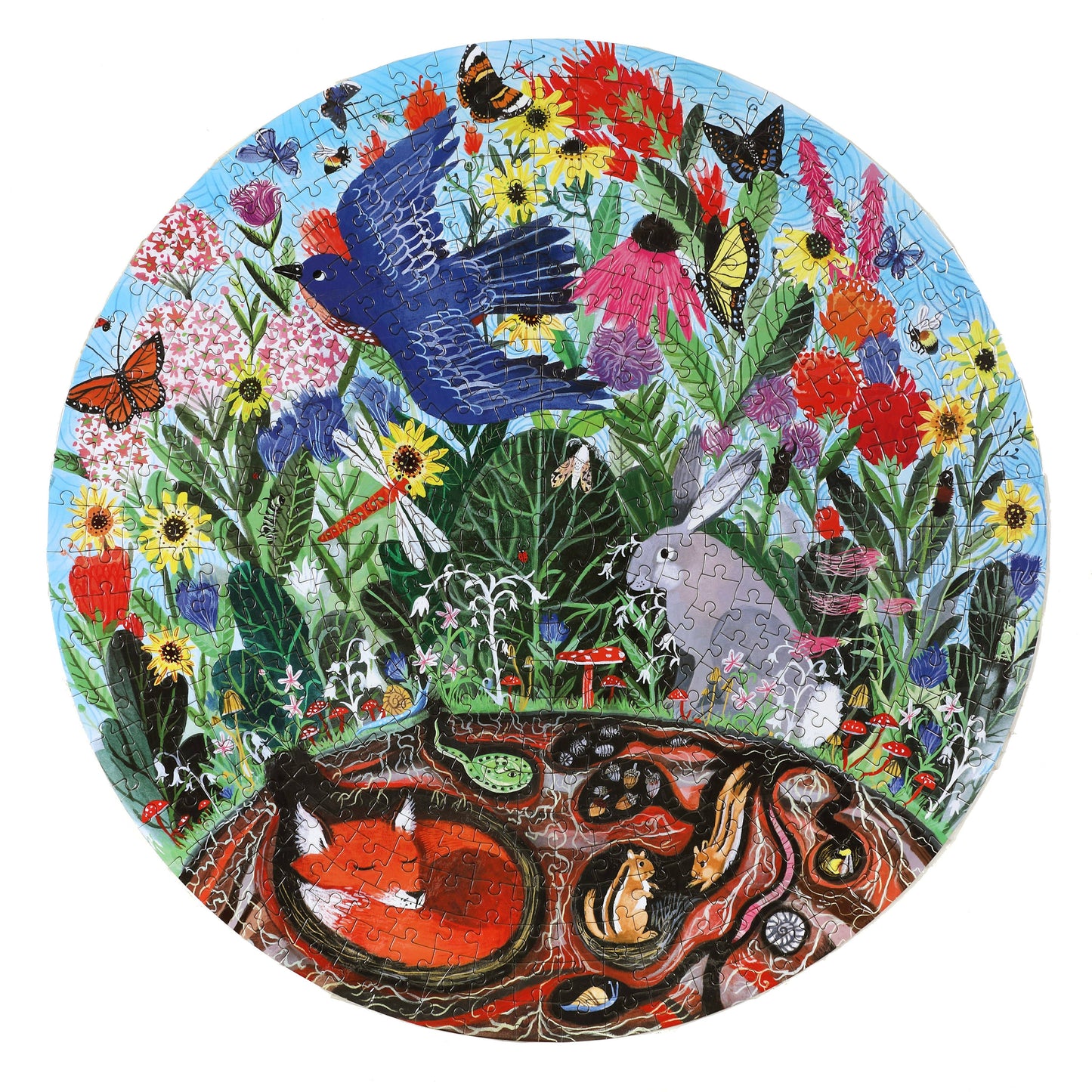 The Rewilding 500 Piece Puzzle features a vibrant meadow scene with flowers, insects, a blue bird in flight, a rabbit, and a fox curled up in an underground den—an enchanting and sustainable jigsaw experience.