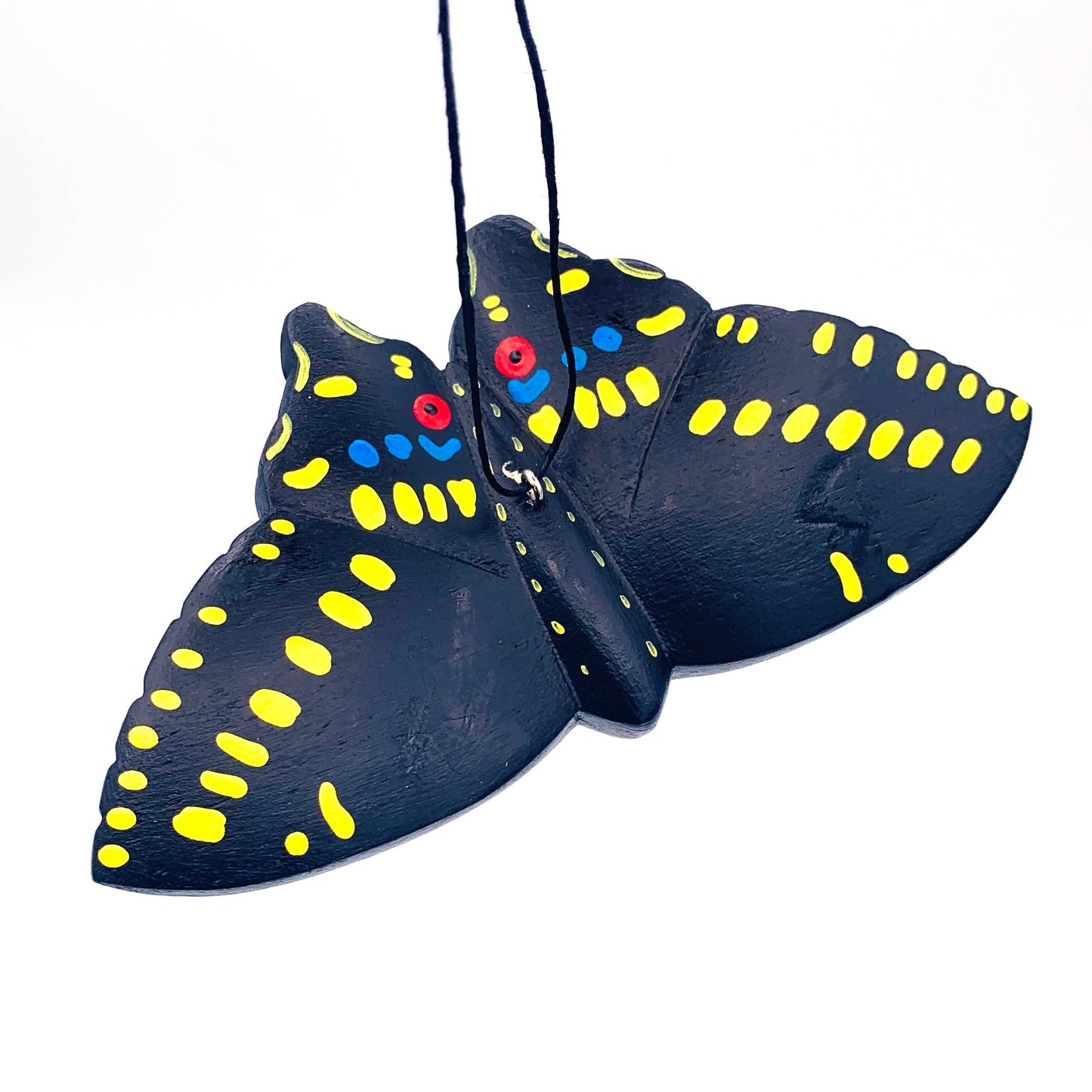 The Black Swallowtail Butterfly Balsa Ornament features hand-carved black balsa wood with yellow spots, blue dots, and red eyes. It hangs by a black string against a white background.