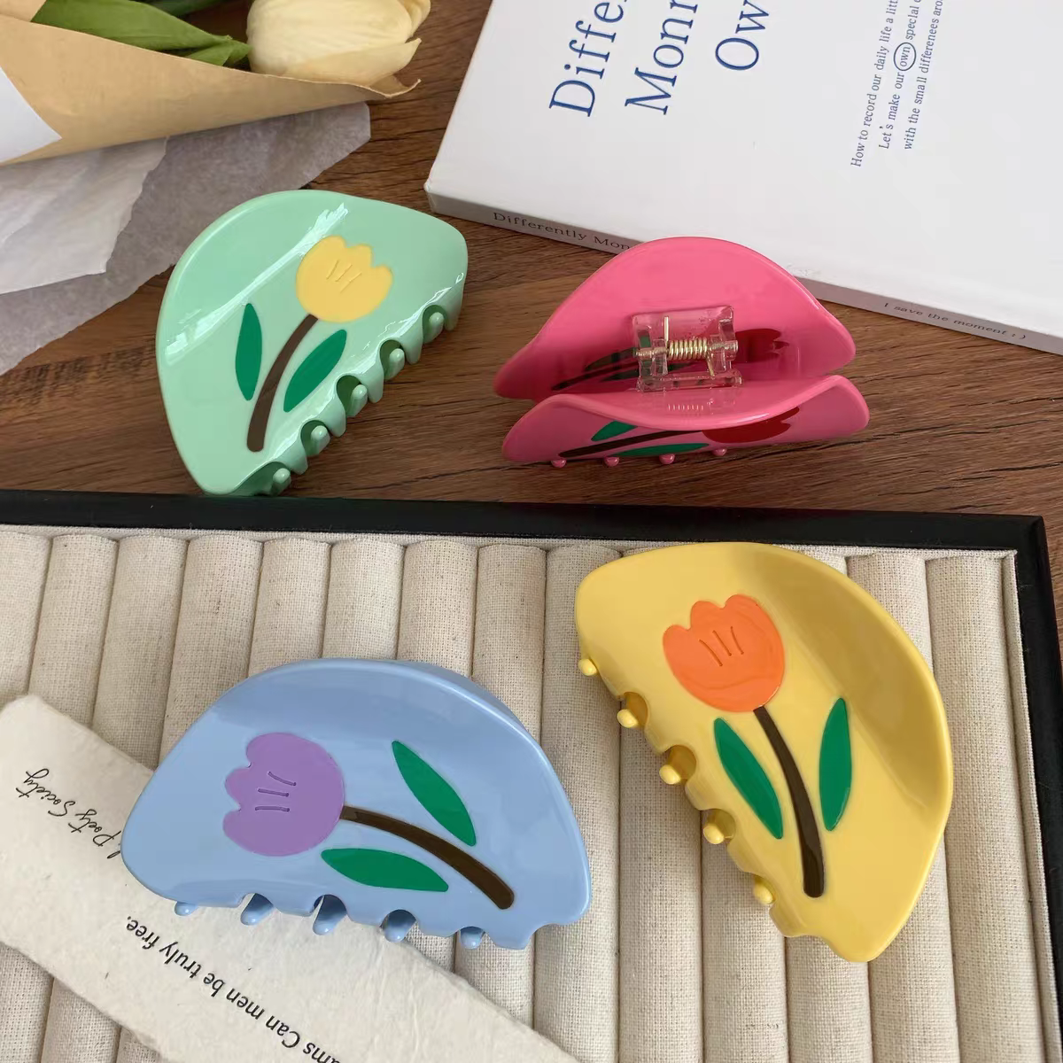 Four curved Tulip Hair Claw Clips in light green, pink, blue, and yellow, each featuring a floral design.