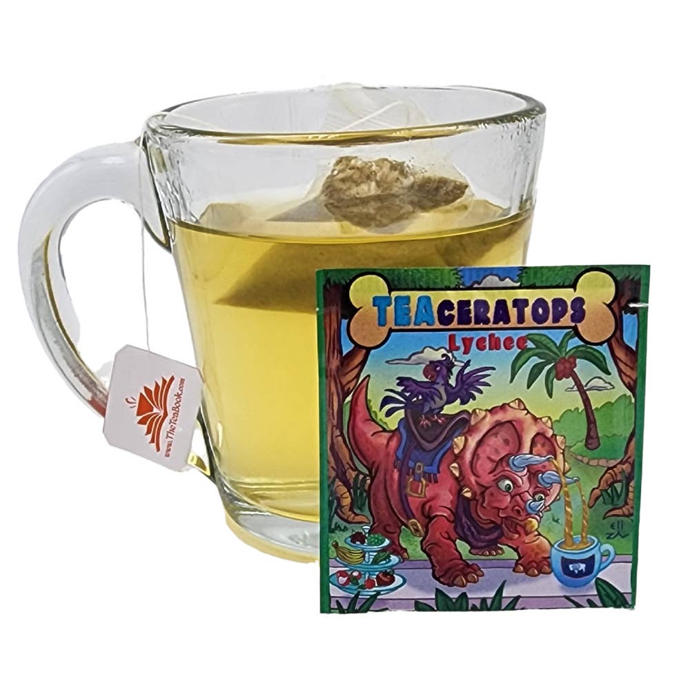 A glass mug of caffeine-free tea with a pyramid bag inside, next to a square packet of TEAhistoric Park Dino Organic Tea Sampler featuring a cartoon triceratops and a bird.