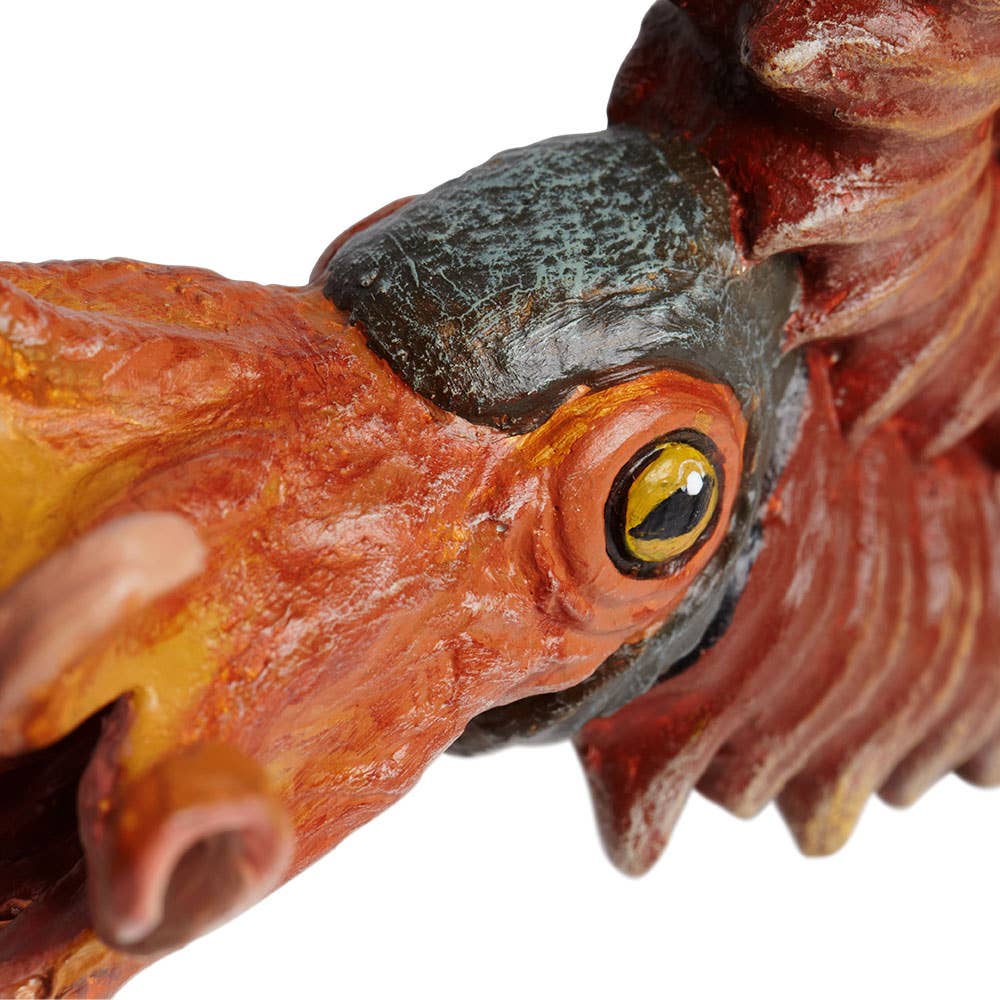 Close-up of the Ammonite Figurine, a colorful and detailed sculpture depicting a prehistoric bird or dinosaur head with textured skin, a yellow eye, and an open beak, featuring a subtle ammonite fossil pattern incorporated into its design.