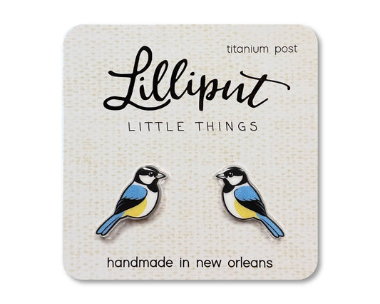 Chickadee Earrings: A pair of bird-shaped, novelty earrings featuring blue, yellow, black, and white details on a card labeled Lilliput Little Things. Handmade in New Orleans with hypoallergenic titanium posts.