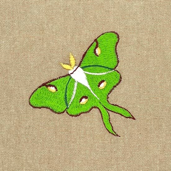 The Luna Moth Field Bag features an embroidered green luna moth with yellow and white details on light brown cotton, making it a perfect addition to any nature lover’s or birdwatcher’s collection.