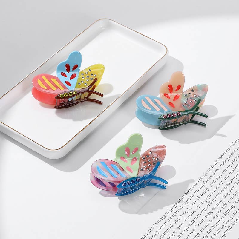 Three blue, yellow, and green Side Butterfly Hair Claw Clips resting on a white ceramic tray.