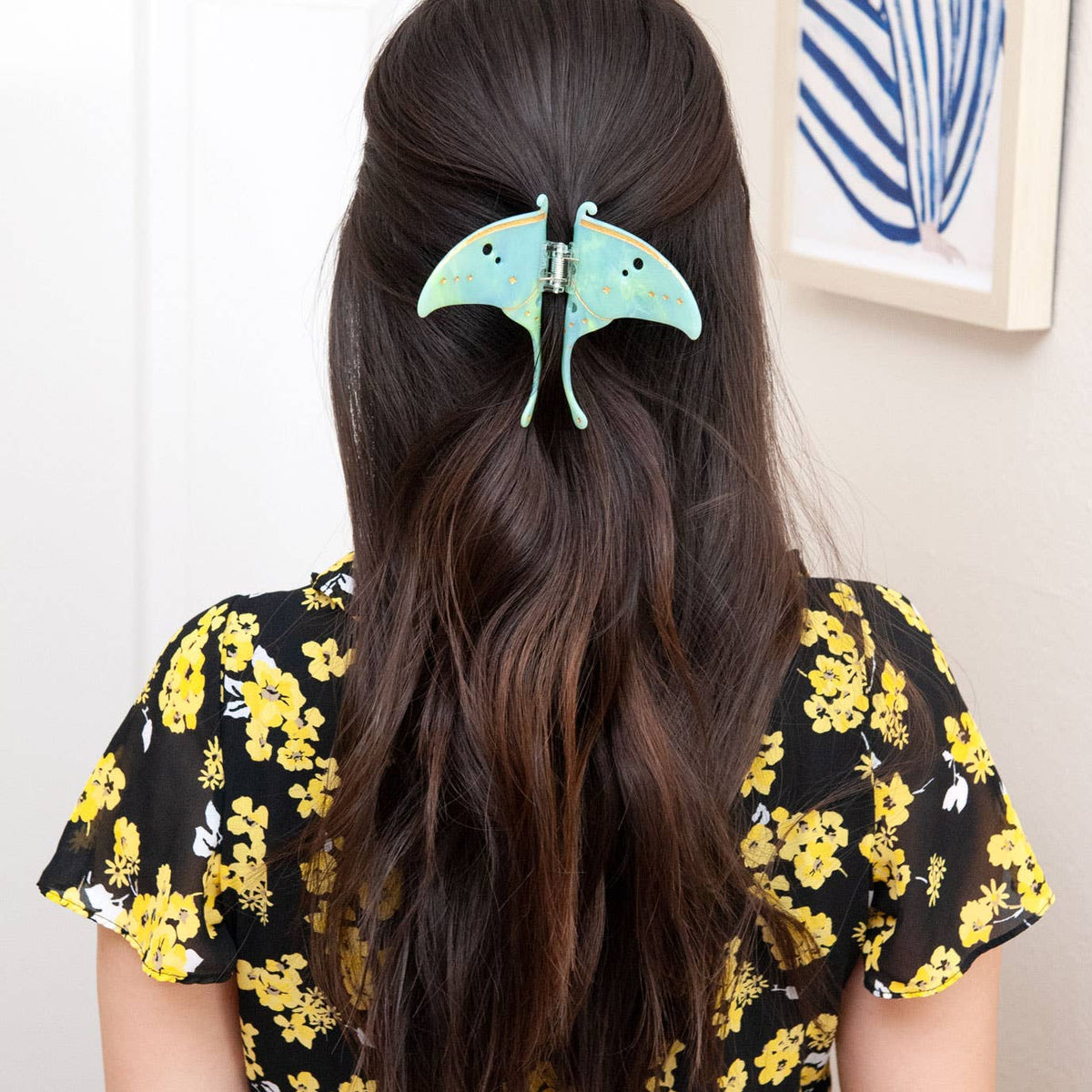 A mint green Luna Moth Hair Claw Clip holding back a section of long, dark hair.