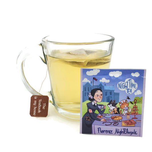 A clear glass mug of Florence NightTEAngle: Organic Night Time Tea sits next to its tea bag envelope, which depicts a woman and two cats having tea, with a tag reading The TeaBook hanging from the mug.