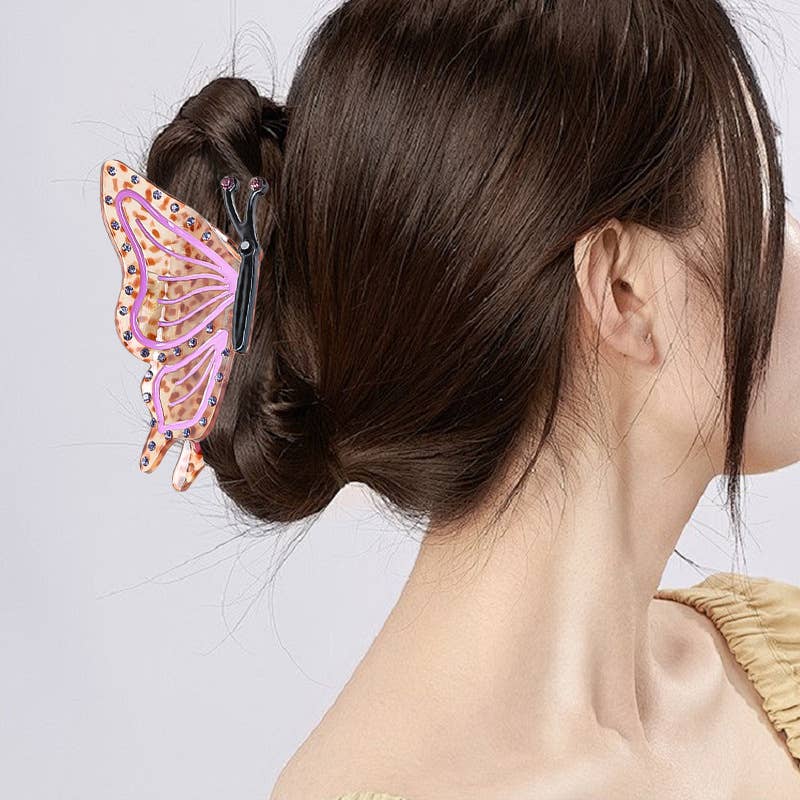A person wears an eco-friendly acetate Butterfly Hair Claw Clip with pink wings and decorative crystals in their bun.