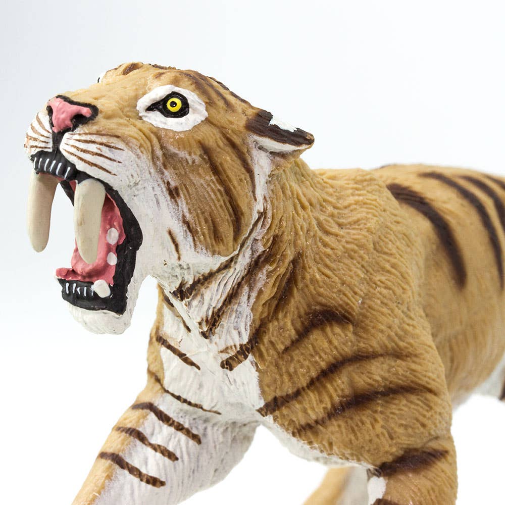 A close-up of the Smilodon Saber-Toothed Cat Figurine Toy, featuring lifelike details inspired by the mighty saber-toothed cat from Rancho La Brea tar pits, with prominent fangs, striking yellow eyes, and realistic brown-striped fur set against a white background.