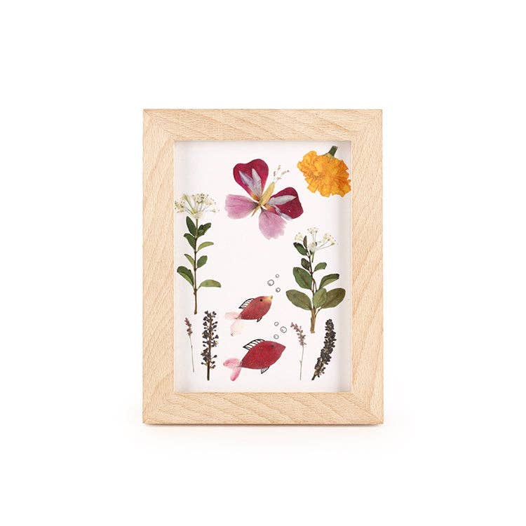 The Huckelberry Pressed Flower Frame features a beechwood frame with pressed flowers and leaves, two illustrated red fish, and bubbles on a white background—ideal for displaying your flower press creations.