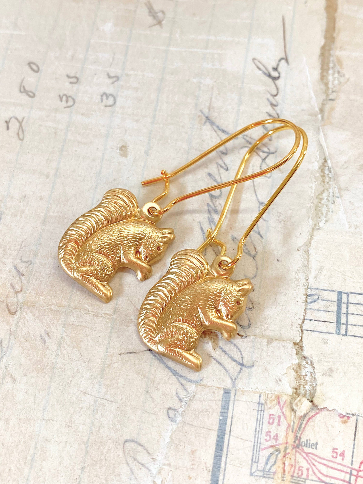 The Woodland Forest Squirrel Earrings are delicately displayed on vintage handwritten paper with faded ink and a torn edge, embodying the playful spirit of woodland jewelry inspired by curious forest creatures.