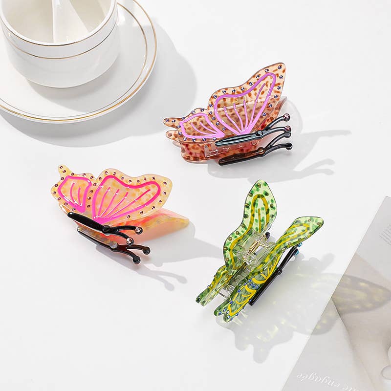 Three Butterfly Hair Claw Clips in orange, pink, and green, crafted from eco-friendly acetate and decorated with small rhinestones.