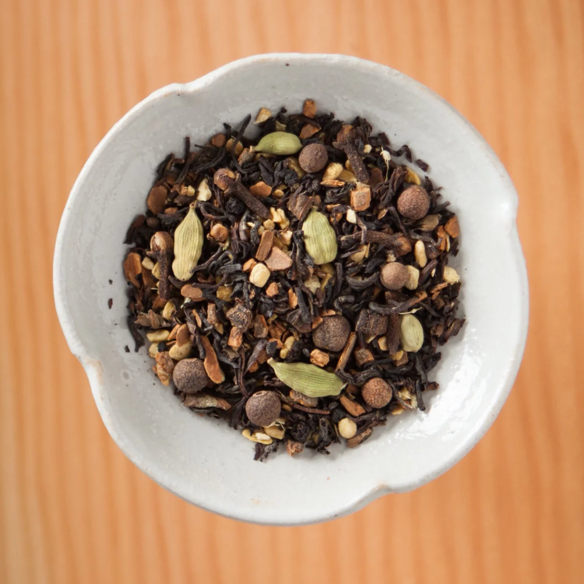 A small white bowl filled with Cedarwood Chai (ORG) – Loose Leaf Tin, featuring a blend of Himalayan black tea, whole cardamom pods, and organic ginger.