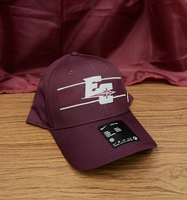 A maroon Nike Club Lightweight Cap featuring a white "E" and star logo on the front, displayed on a wooden surface with a maroon fabric backdrop.