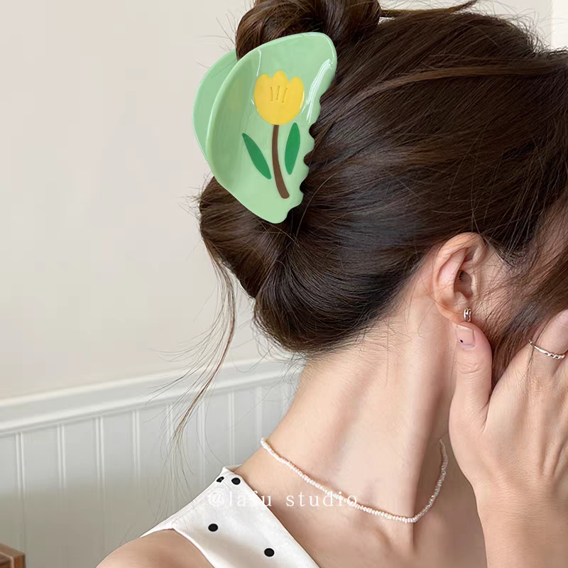 A person with dark hair pulled up in a bun secured with a light green Tulip Hair Claw Clip.