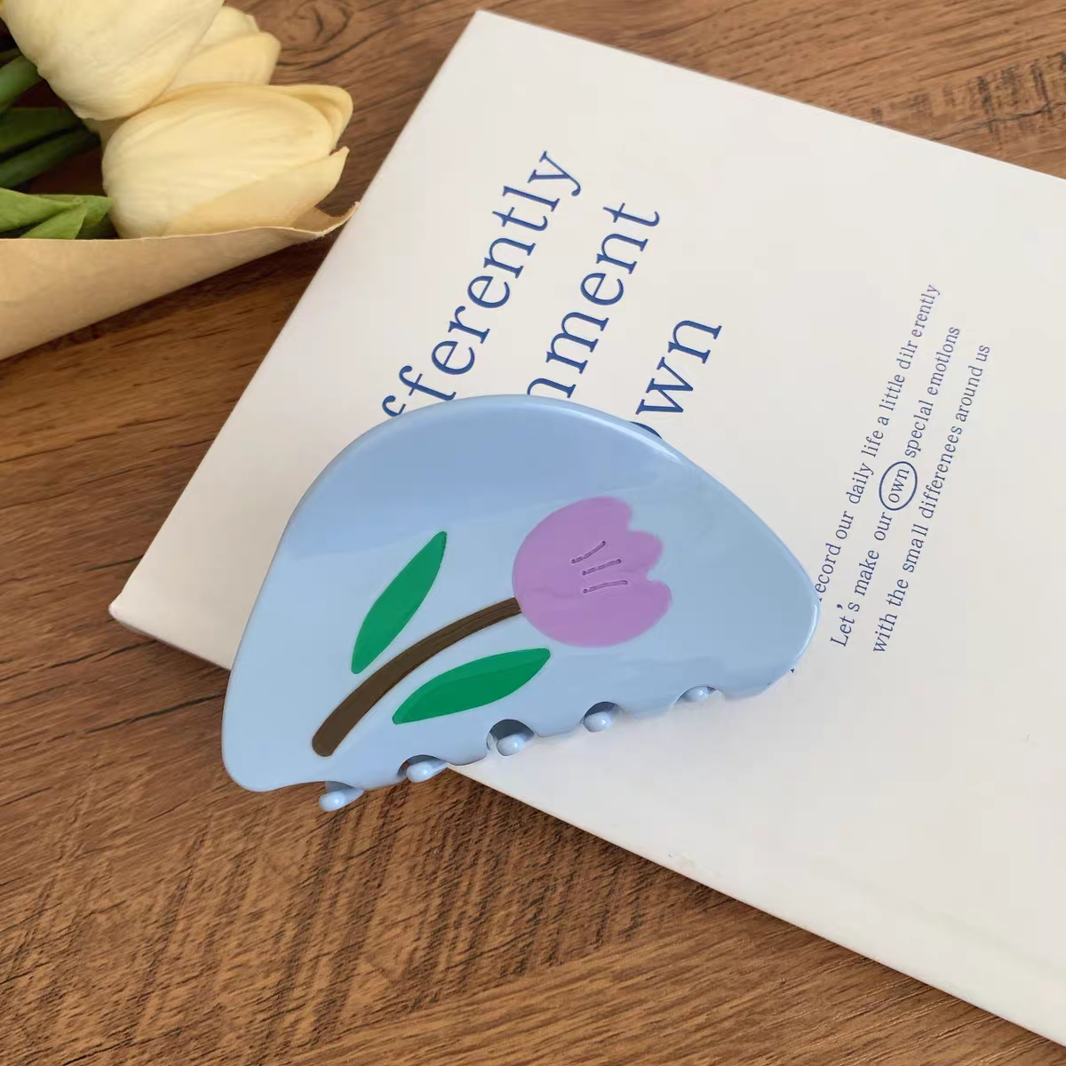 Light blue semi-circular Tulip Hair Claw Clip resting on an open book.