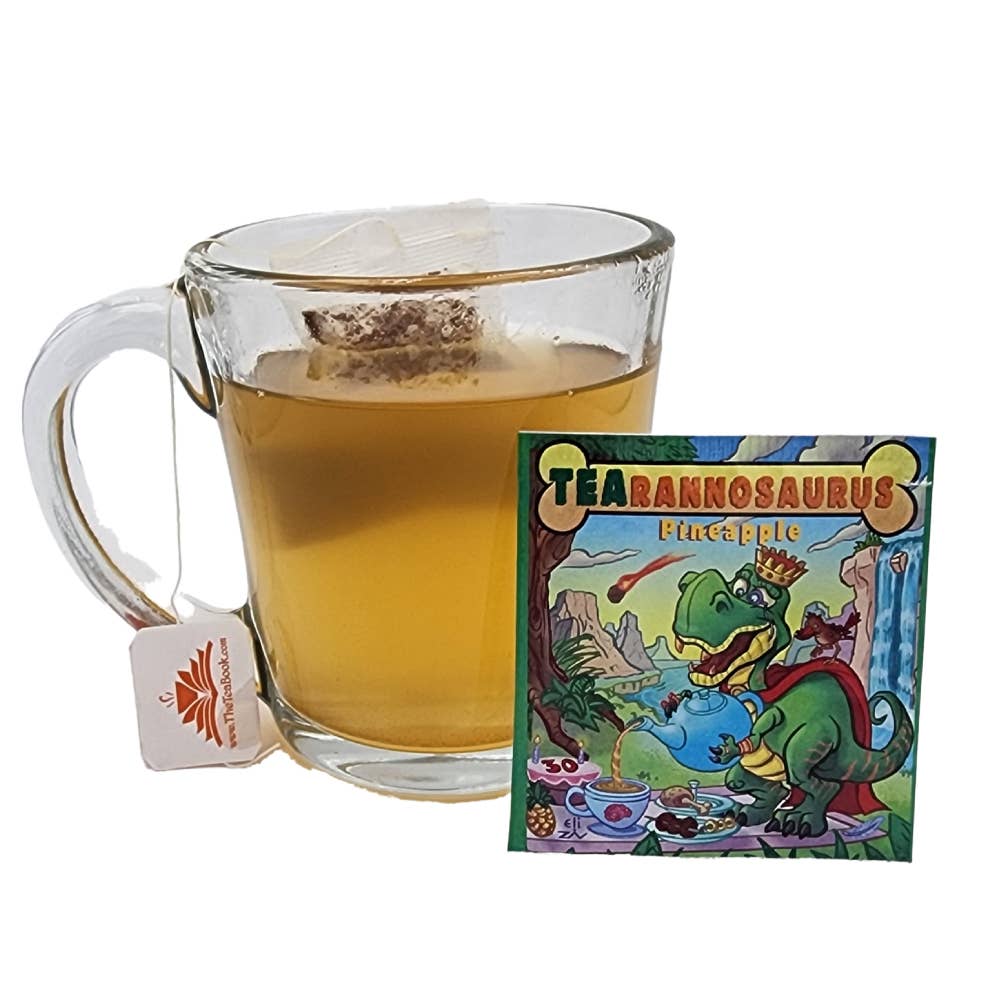 A glass mug of caffeine free tea next to a TEAhistoric Park Dino Organic Tea Sampler packet illustrated with a T-Rex drinking dinosaur tea.