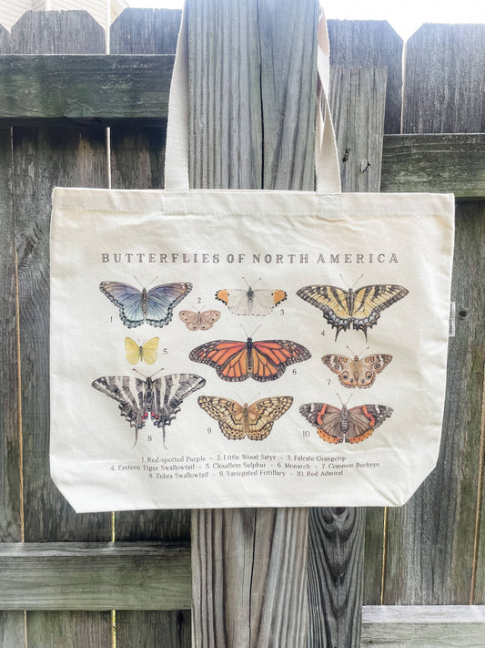 The Feed & Dwell Butterflies of North America Large Organic Cotton Tote Bag, GOTS-certified, displays watercolor butterflies and numbered names of ten North American species on its front with “Butterflies of North America” at the top.