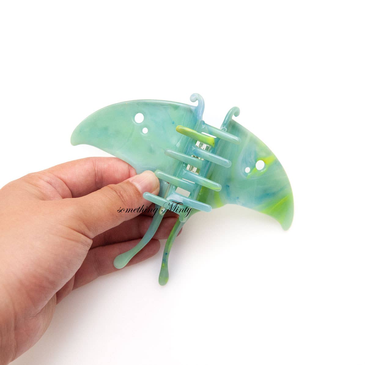 A hand holds a mint green and blue Luna Moth Hair Claw Clip shaped like a moth.