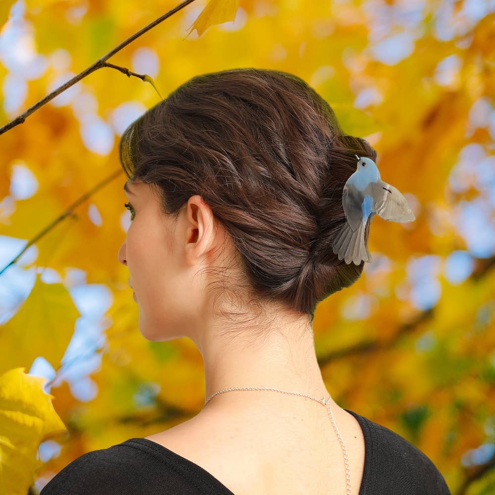 A person with a brown hair bun styled with a Blue and Gray Bird Hair Claw Clip.