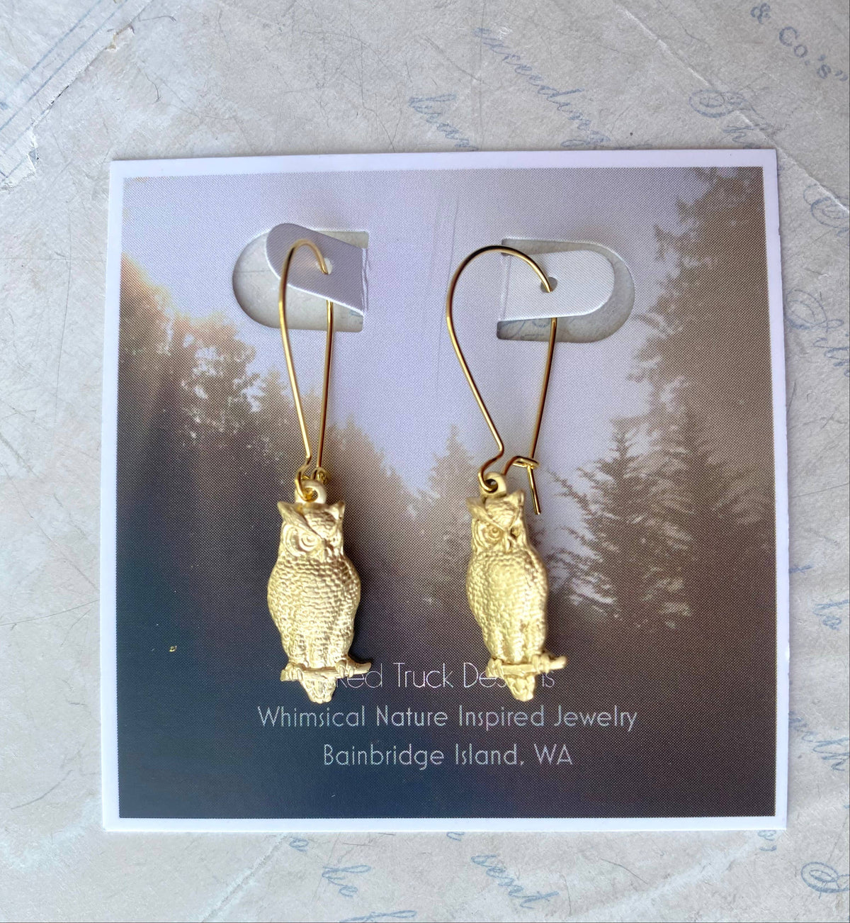Wise Owl Earrings displayed on a card that reads, Whimsical Nature Inspired Jewelry, Bainbridge Island, WA, with a forest background. These vintage earrings beautifully capture the charm of woodland style.