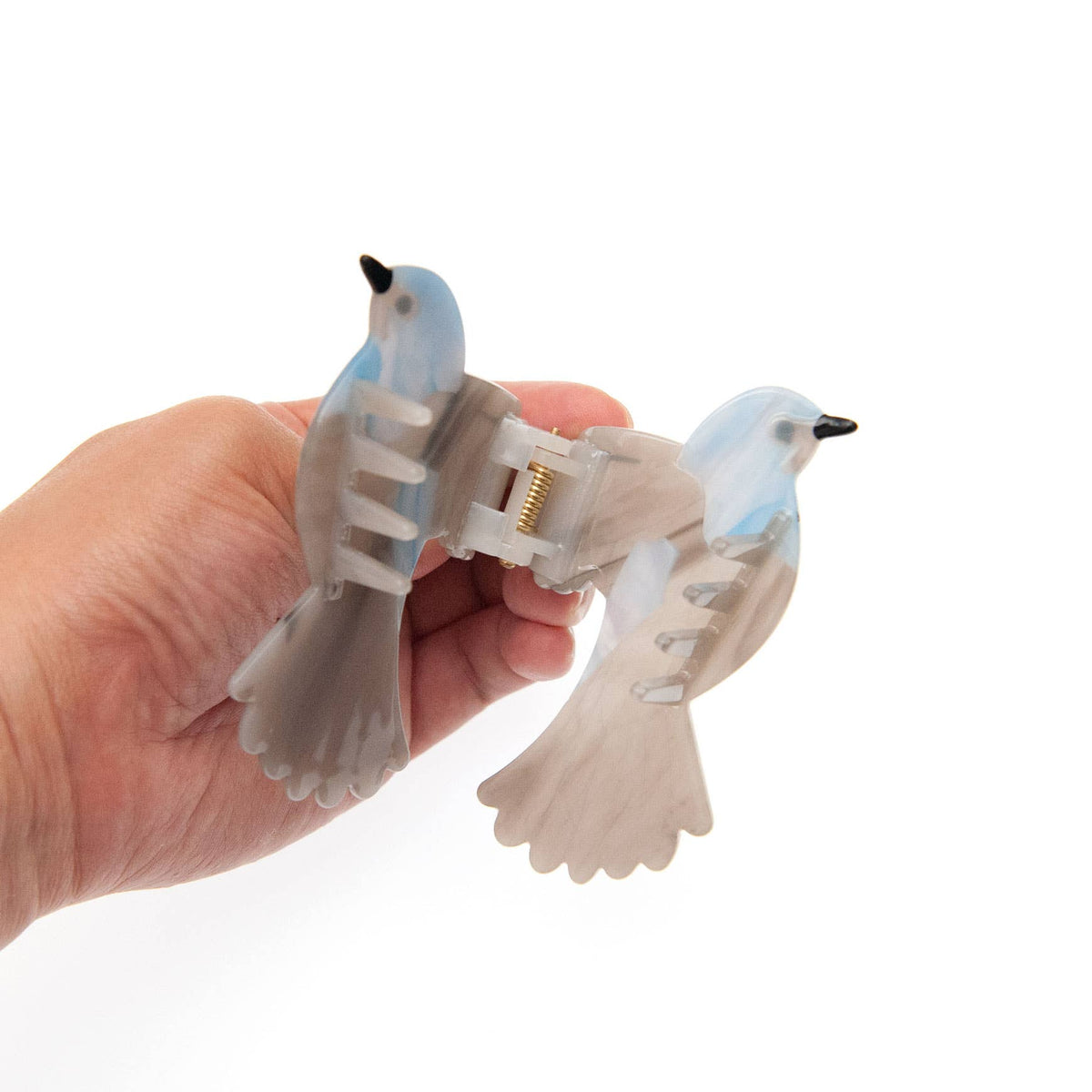 A hand holding a Blue and Gray Bird Hair Claw Clip with blue and gray marbled detail.