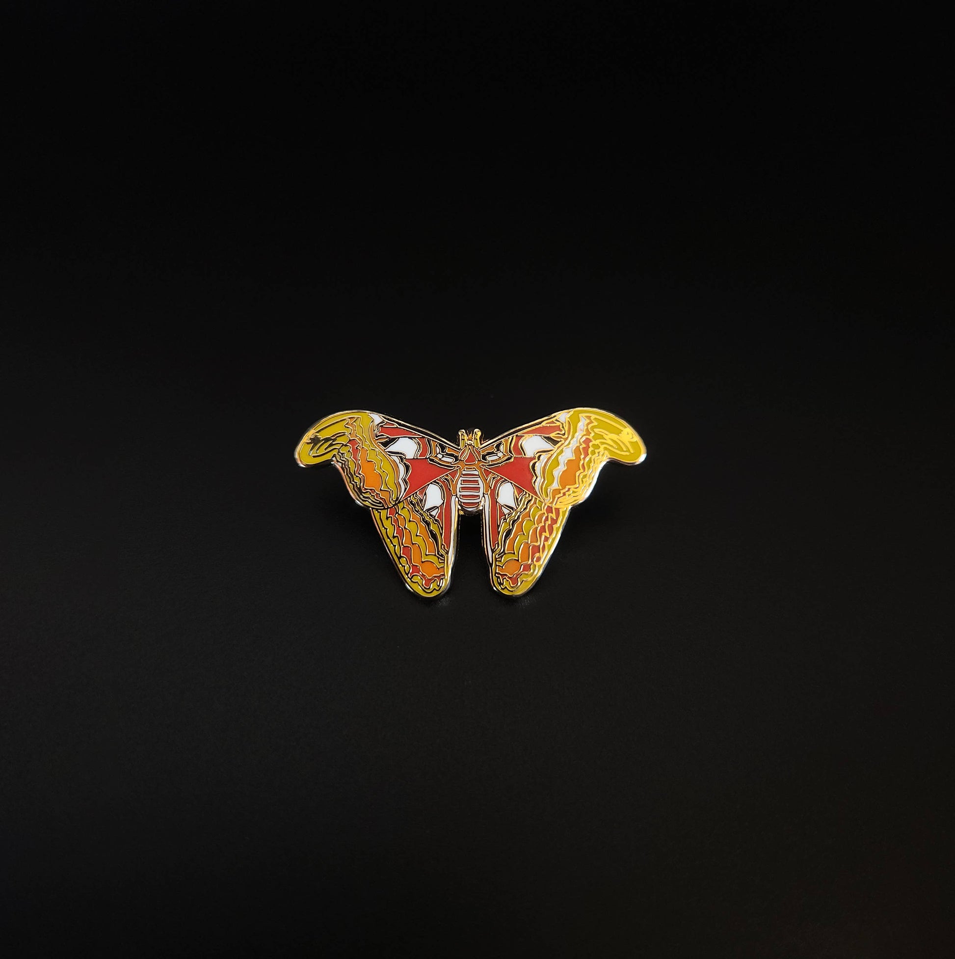 The Atlas Moth Educational Insect Enamel Pin, featuring vibrant yellow, orange, and red patterns, is displayed centered on a solid black background.