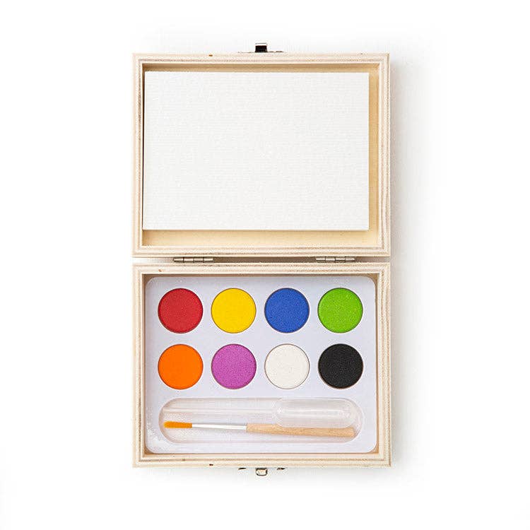 The Huckleberry Landscape Paint Kit is an open wooden box that includes a small blank canvas, eight round watercolor paints in assorted colors, a paintbrush, and a compact mini watercolor paint set.