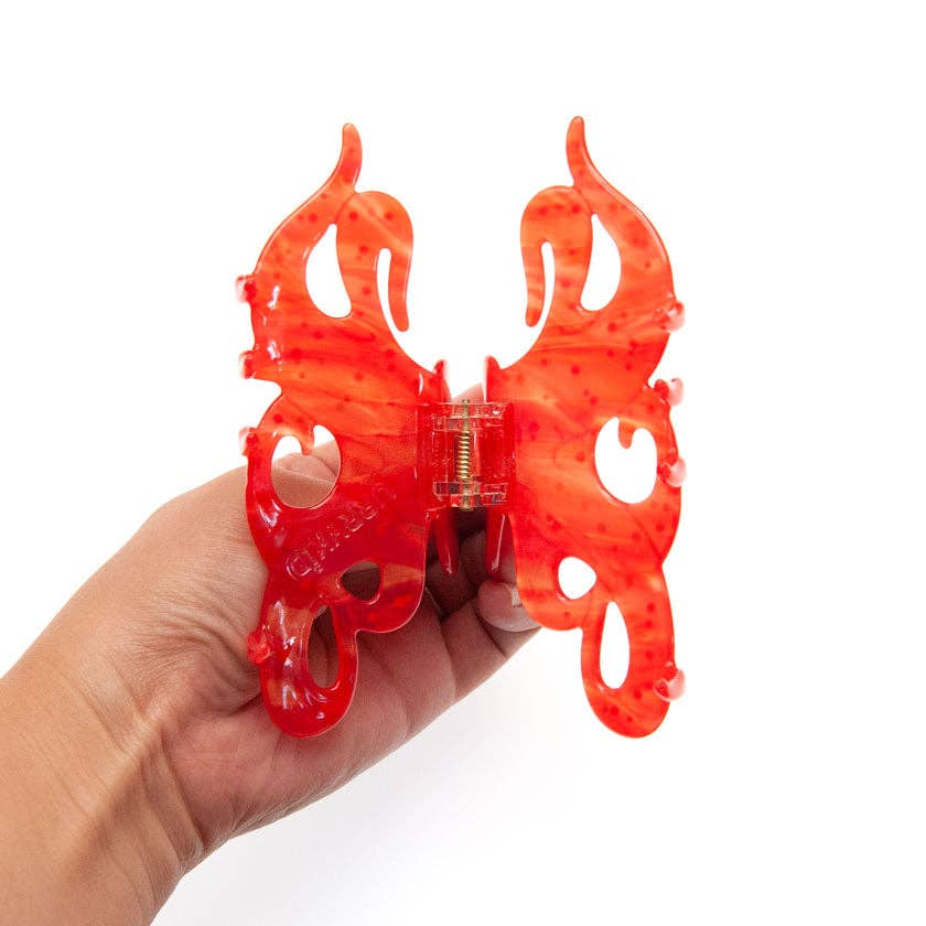 A hand holding a translucent red butterfly-shaped Octopus Claw Clip made of cellulose acetate.