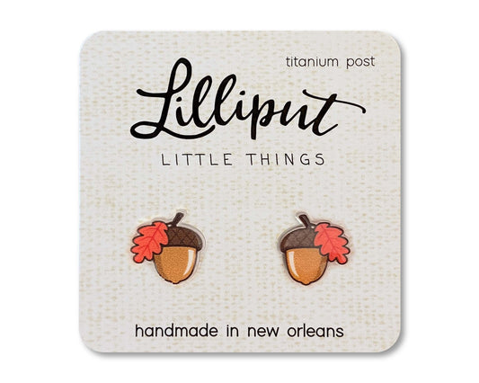 The Fall Acorn Earrings are a pair of acorn-shaped handmade earrings with red leaves, displayed on a card labeled Lilliput Little Things. Crafted in New Orleans, they feature hypoallergenic titanium posts.