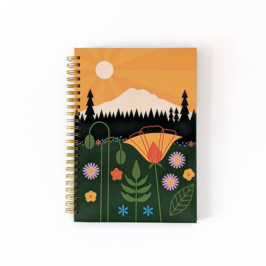 Mount Rainier Spiral Notebook with a matte hardcover, featuring a colorful illustration of a sun rising over a mountain, forest, and wildflowers, finished with a gold spiral binding.