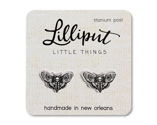 A pair of Death’s Head Moth Earrings, featuring hypoallergenic titanium posts and handmade in New Orleans, displayed on a card labeled Lilliput Little Things.