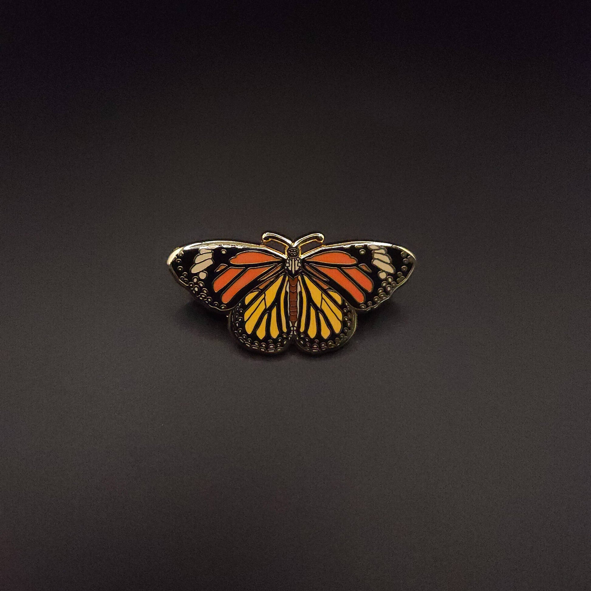 The Monarch Butterfly Educational Insect Enamel Pin, featuring vibrant orange, black, and white details, is centered against a plain black background.