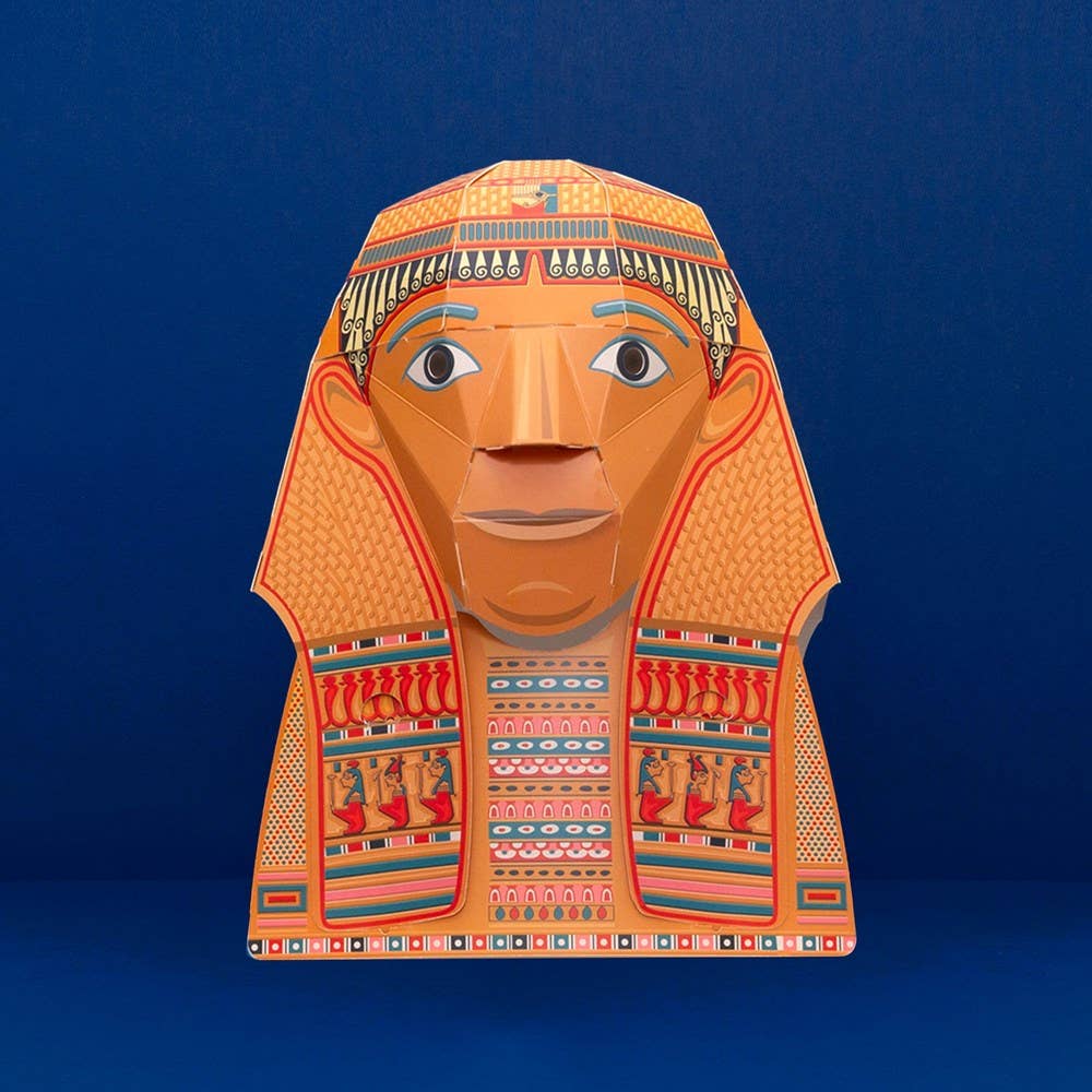 The Create Your Own Egyptian Head Mask features a pharaoh design with ornate geometric patterns, a headdress, and expressive eyes—a vibrant educational addition—shown on a plain dark blue background.