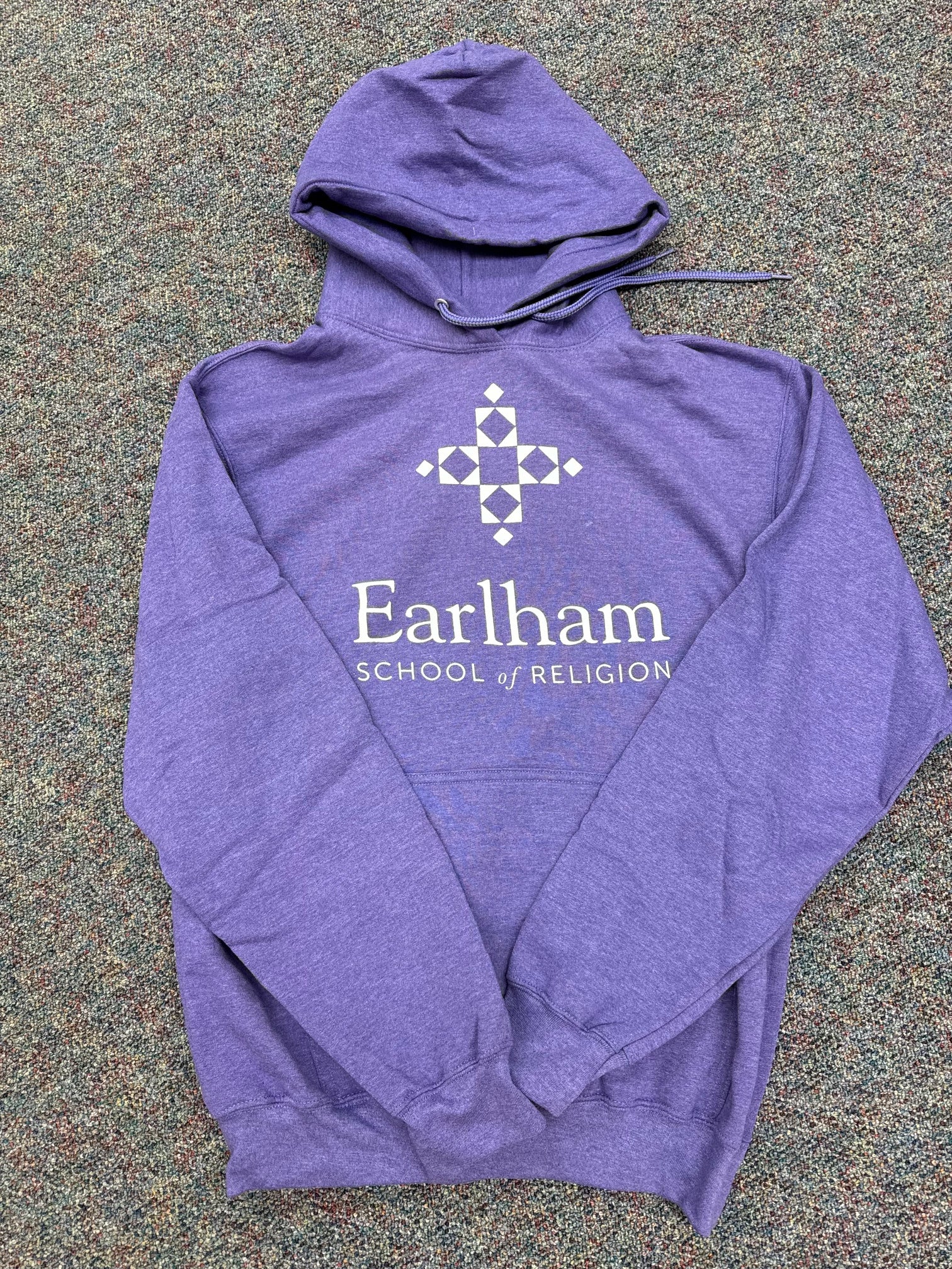 The ESR Pullover Hoodie is a purple hooded sweatshirt featuring "Earlham School of Religion" and a geometric cross logo in white on the front, displayed flat on a speckled carpeted floor.