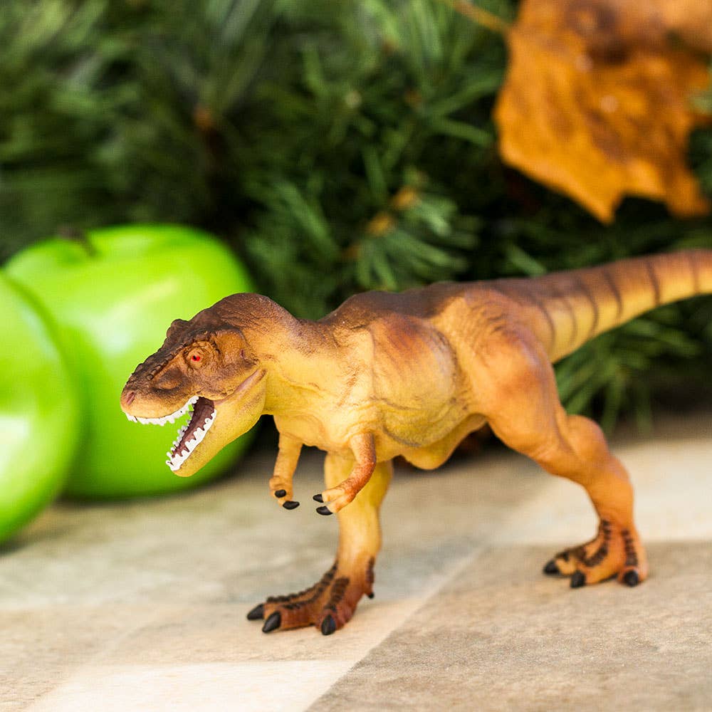 The Tyrannosaurus Rex Kids' Figurine Toy, designed as a realistic and fierce theropod dinosaur, stands on a surface near two green apples with lush foliage in the background.