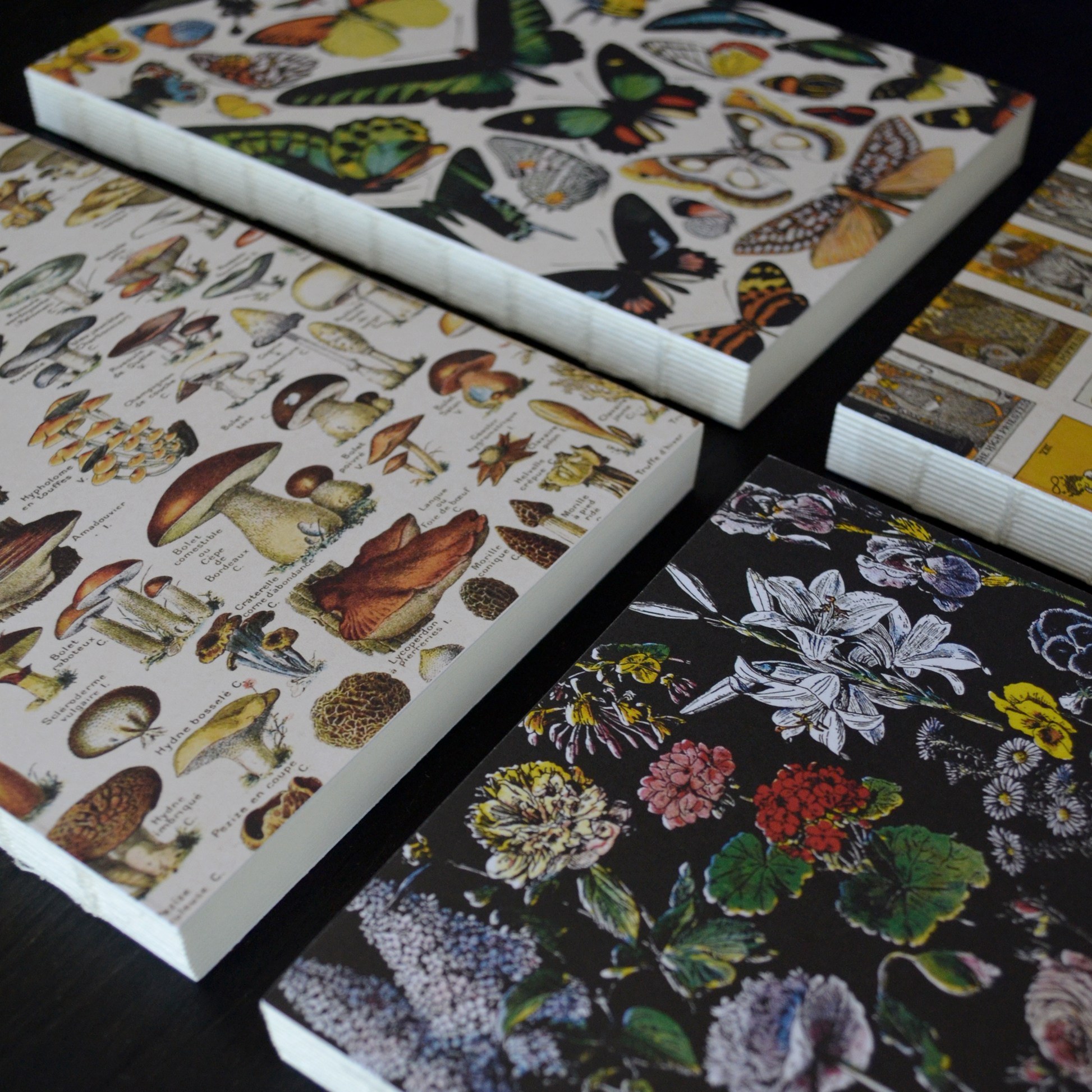 The Vintage Botanical Flower Garden Exposed Binding Notebook includes four stacks of paper with vintage-style butterflies, mushrooms, wildflowers on black, and assorted botanical and insect illustrations—ideal for journaling. Edges are neatly aligned.