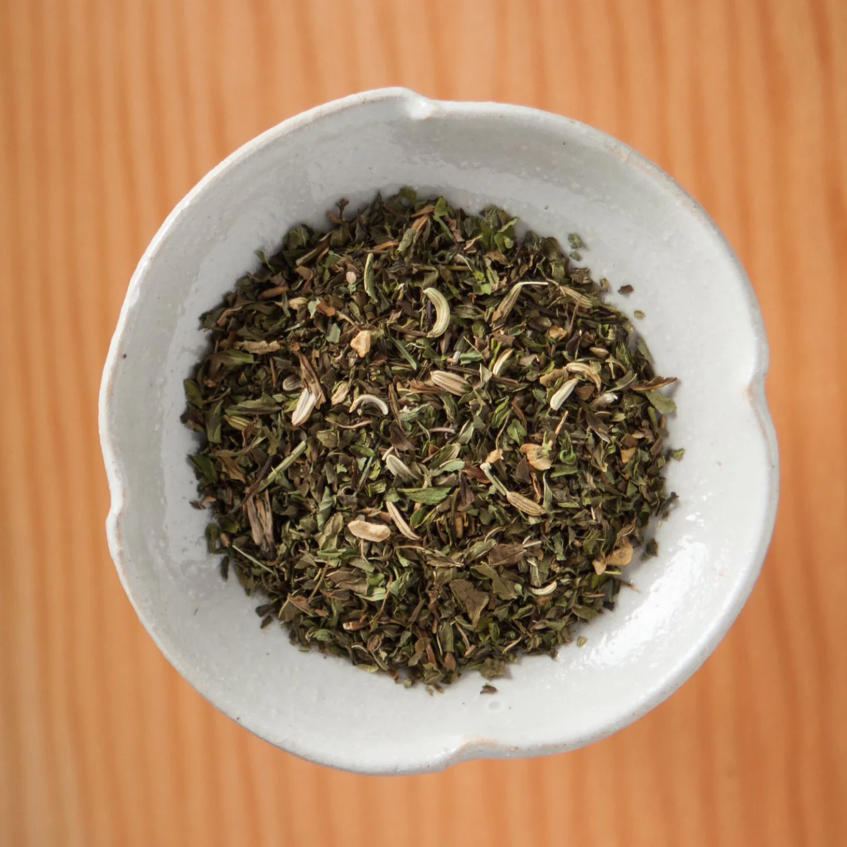 A small, scalloped white bowl filled with Twilight Mint (ORG) – Loose Leaf Tin organic loose-leaf peppermint tea.