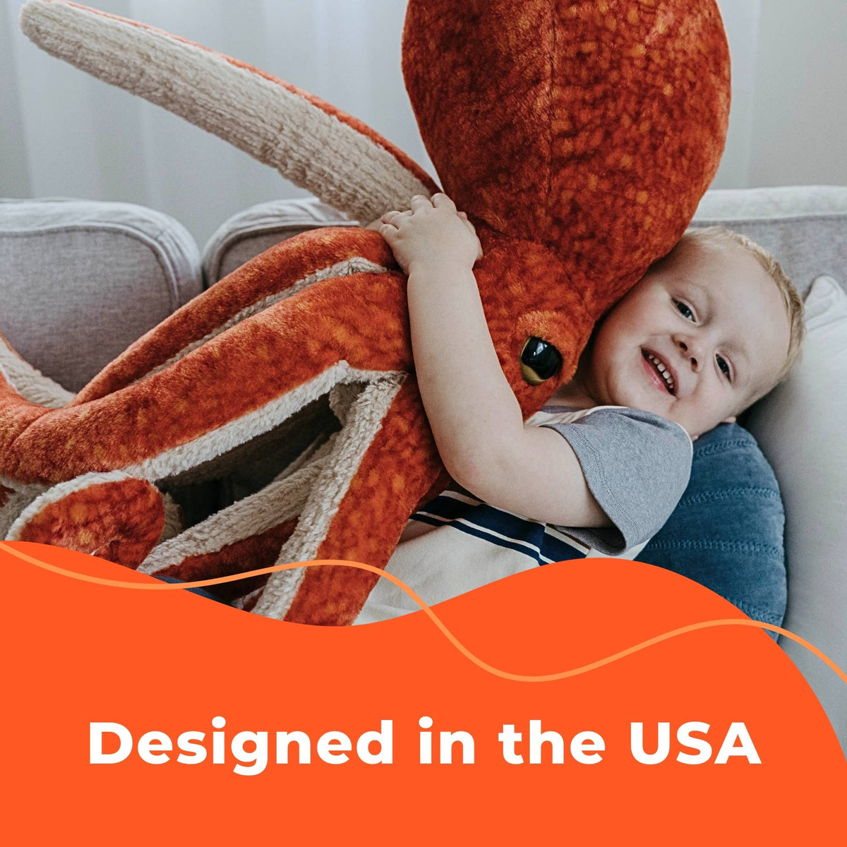 A smiling child cuddles a small, realistic Wild Onez Highland Cow 9″ plush on a couch. Text at bottom reads, Designed in the USA.