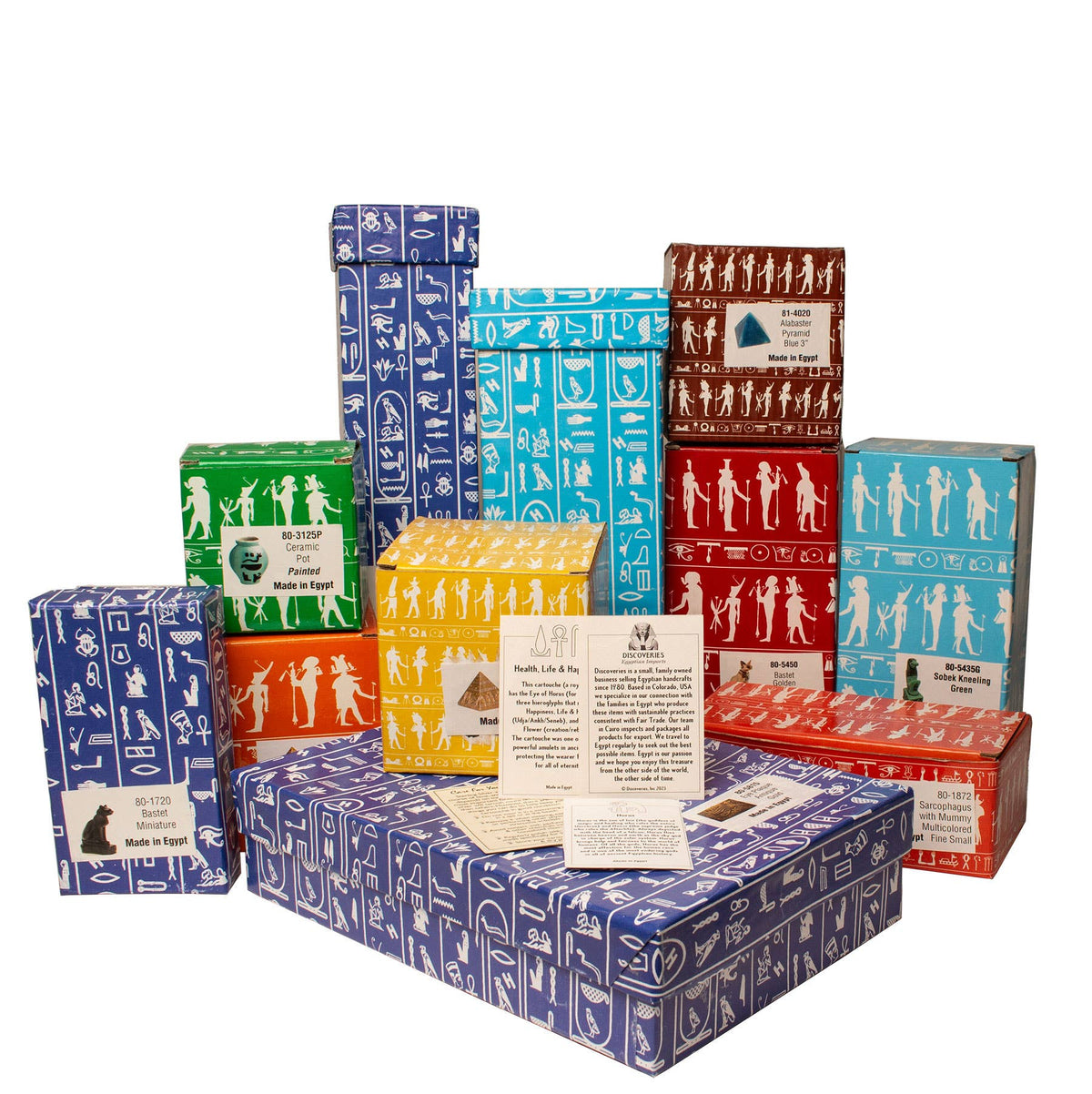 A collection of vibrant rectangular boxes, each adorned with repeating white Egyptian-style illustrations and symbols, is arranged in neat rows. In front of the boxes, three cards featuring text and graphics are displayed. Each box captures the mysterious allure of ancient Egypt and suggests hidden treasures inside—perhaps even a small 2.25″ Alabaster Pyramid made in Egypt.