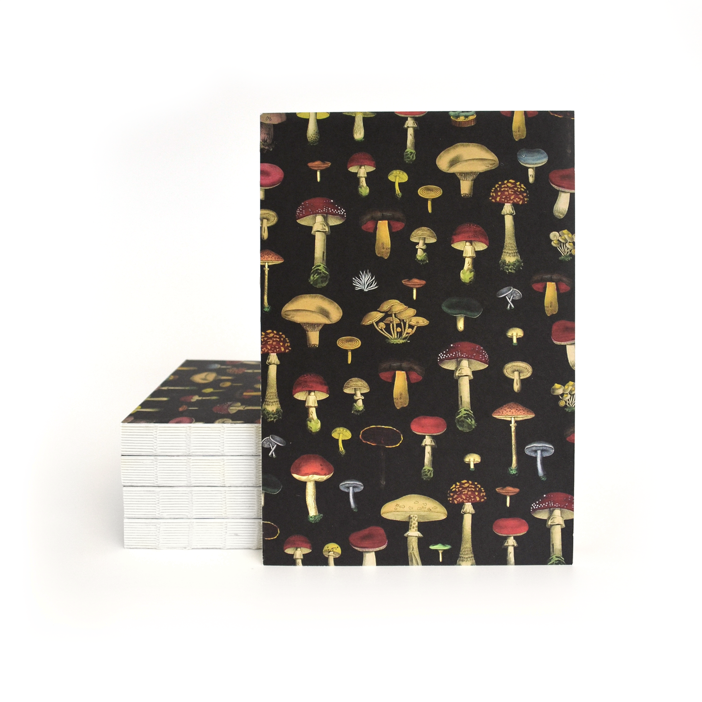 A stack of Vintage Black Mushroom Exposed Coptic Binding Notebooks with covers featuring colorful mushroom illustrations on a black background; one notebook stands upright in front of the stack.