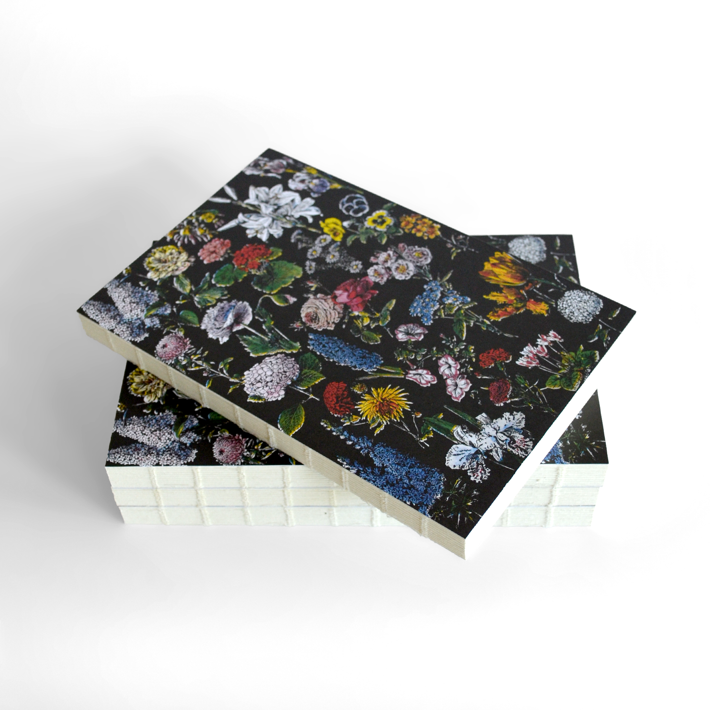 Two hardcover Vintage Botanical Flower Garden Exposed Binding Notebooks with dark covers and colorful floral patterns are stacked on a white surface. The top notebook is slightly askew, revealing the binding and edges of both.