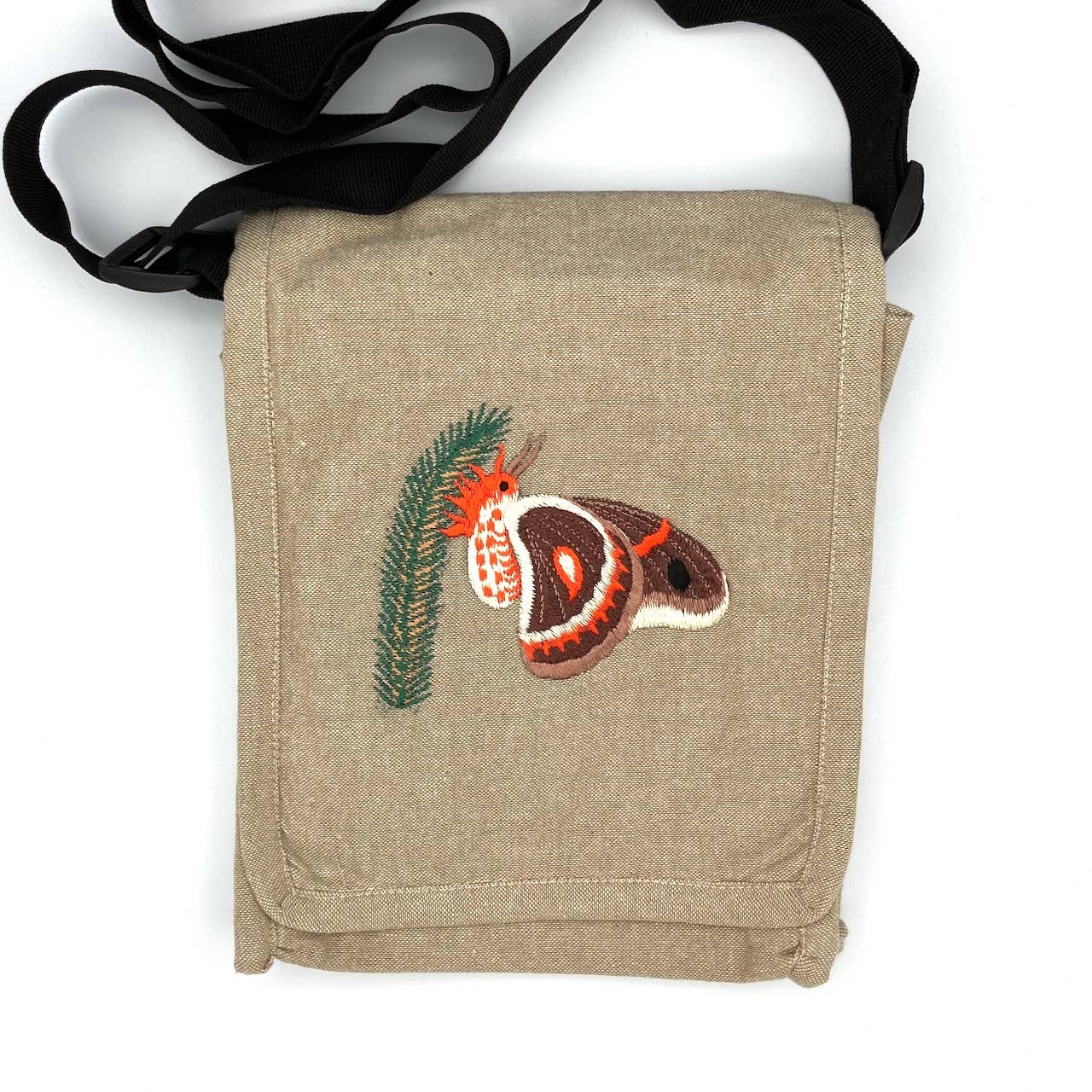 The Cecropia Moth Field Bag is a beige handmade cotton crossbody with a black strap, featuring embroidered brown and orange moth and green pine needle designs—an ideal fair trade accessory for nature lovers.