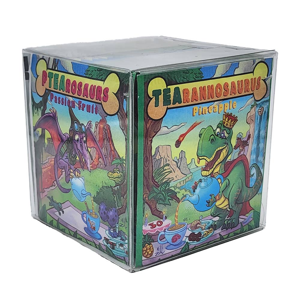 A clear plastic cube box from the TEAhistoric Park Dino Organic Tea Sampler, featuring a Ptearosaurs Passion Fruit box with a pterosaur and a Tearannosaurus Pineapple box with a crowned dinosaur.
