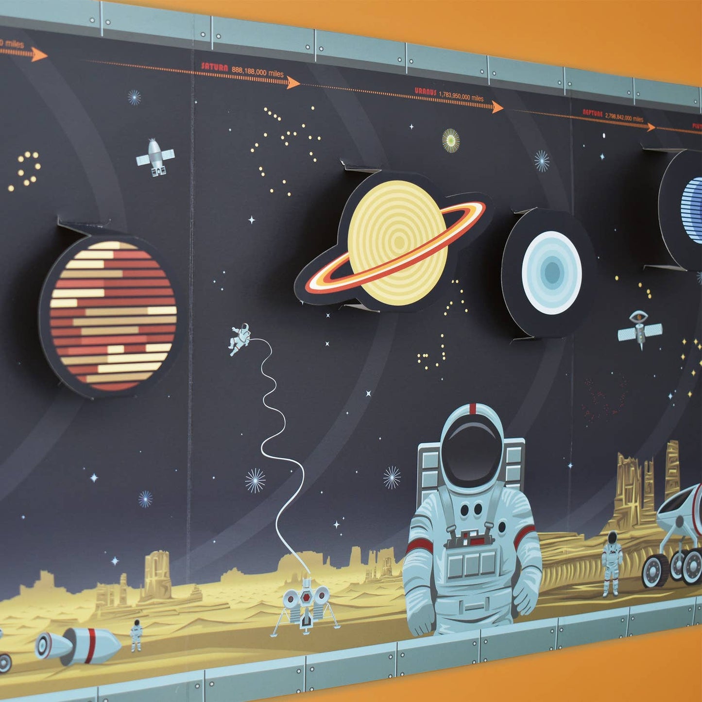 The "Create Your Own Solar System" wall chart features a colorful, illustrated solar system with planets, a satellite, rockets, astronauts on a yellow rocky alien landscape, and vibrant orange details set against a dark starry background.