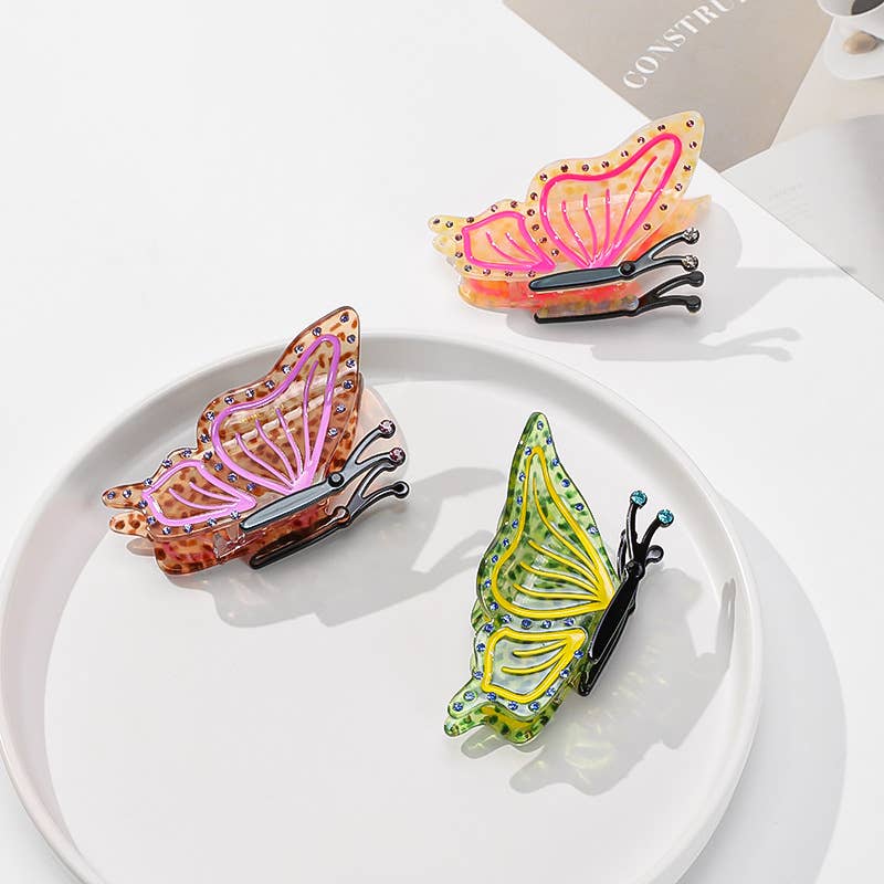 Three Butterfly Hair Claw Clips in yellow, orange, and brown, crafted from eco-friendly acetate and arranged on a white plate.